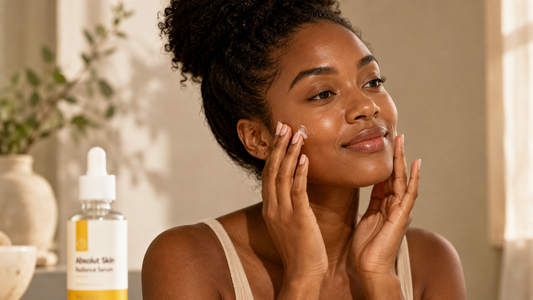 A person with dark skin applies serum with fingertips as part of a brightening skincare routine, with a bottle of Absolut Skin Radiance Serum visible in the foreground