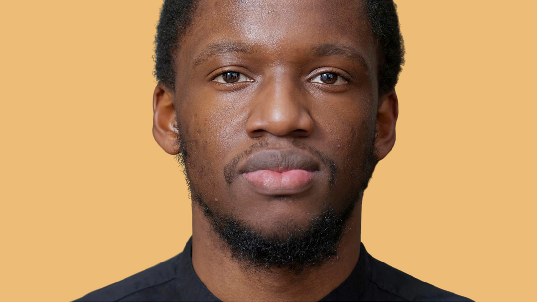 Person with deep skin tone looking at camera with a warm, natural expression against a light background